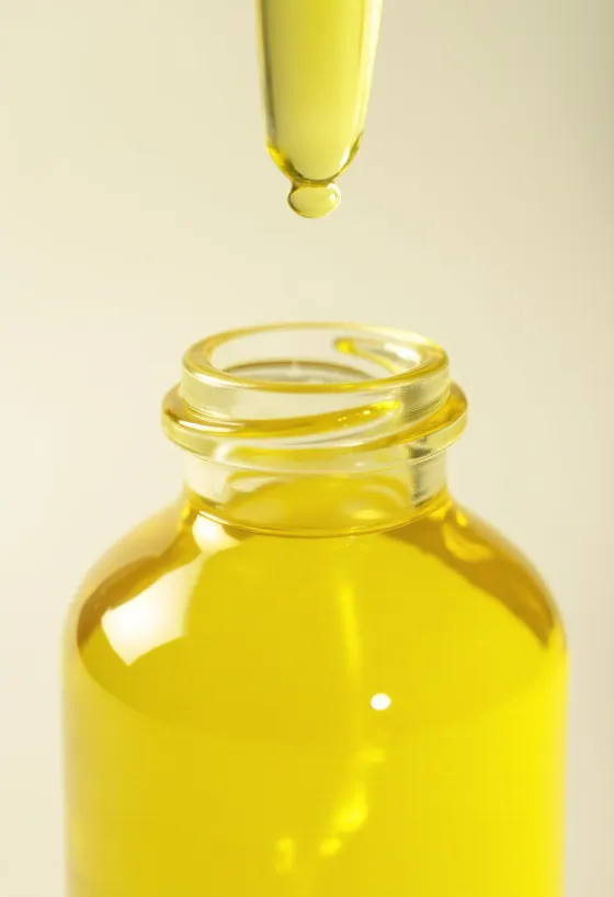 Citronolie i lille flaske, ved siden af friske citronskiver og revet skal